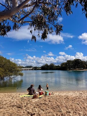A beach with people sitting on a blanket, a tree, and a calm lake. - Stylish Private 2BR Guest Suite Near Beach, Cafés & Creek (Currumbin Waters)