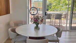A dining area with a round table, four chairs, a vase with flowers, and a hanging light fixture.