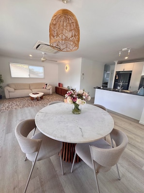 A modern kitchen with a built-in fridge, a dining area with a round table and chairs, and a living room with a sofa and a coffee table.