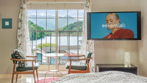 Una habitación de hotel con un ventanal grande, una cama, un televisor y una pequeña mesa con sillas.