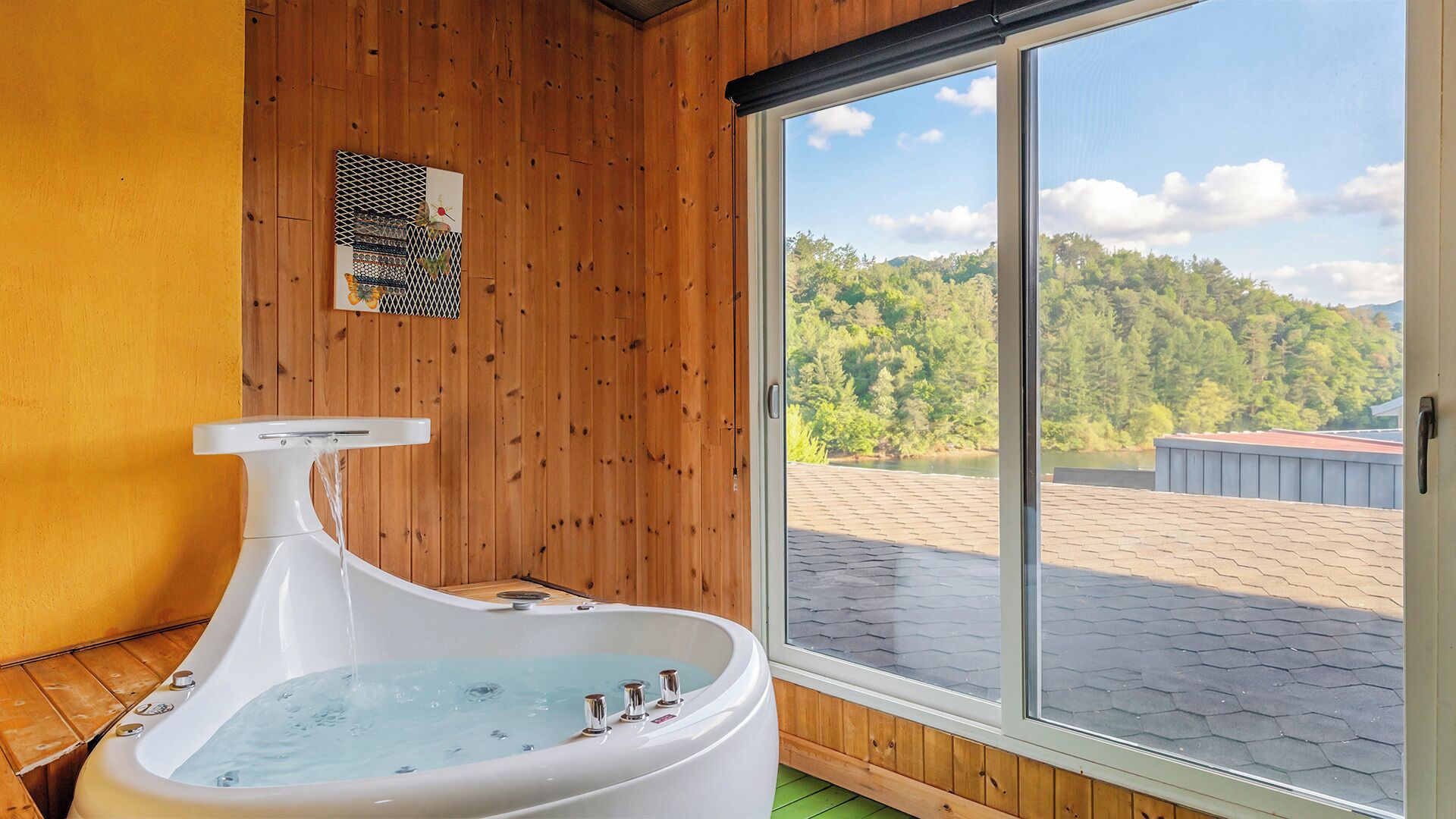 A wooden interior with a hot tub, a window with a view of a forest, and a door.