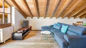 Un salon moderne avec un plafond en bois, un canapé d’angle, un téléviseur à écran plat et une table basse blanche.