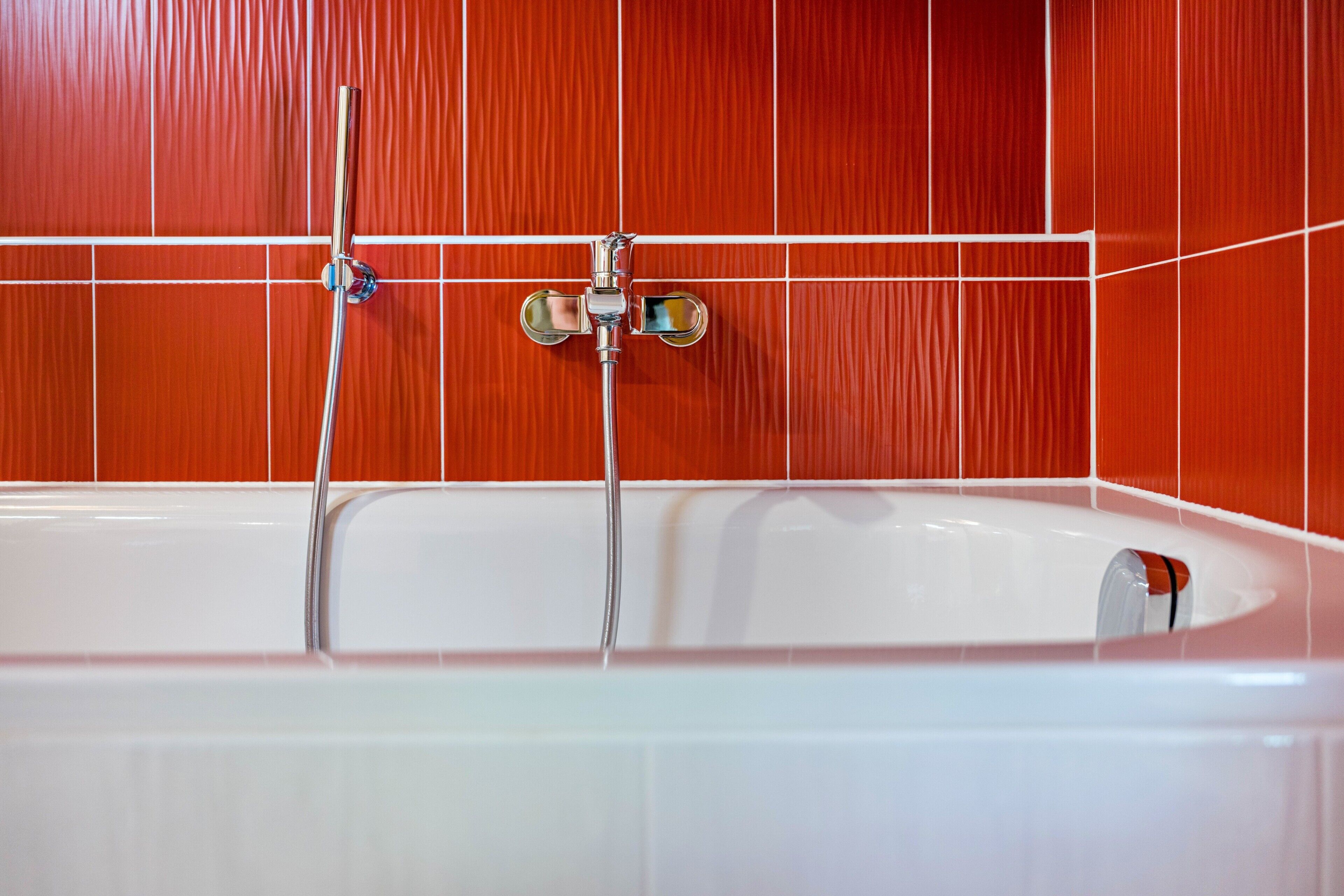 A bathtub with a showerhead and two faucets, set against a tiled wall.