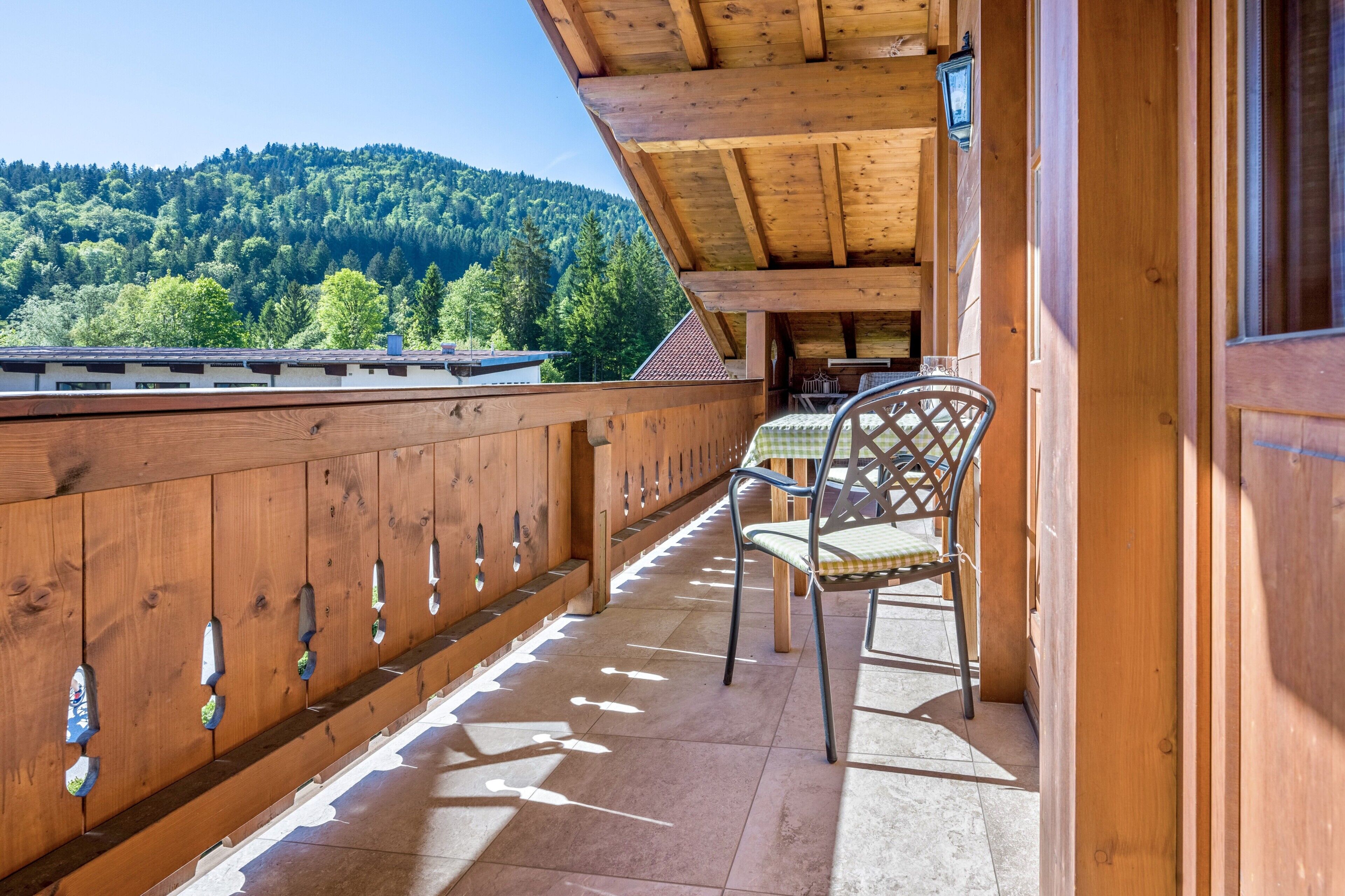A wooden balcony with a table and chair, overlooking a forested hillside.