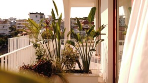 Un balcón con plantas, una barandilla y vistas a edificios al fondo.
