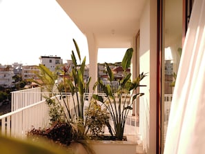 Uma varanda com plantas, corrimão e vista para edifícios ao fundo.