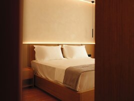 Una cama bien hecha con sábanas blancas y un plaid marrón, cabecera de madera y mesitas de noche.