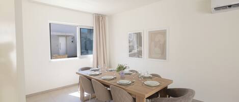 A dining area with a wooden table set for four, beige chairs, and a window with curtains.