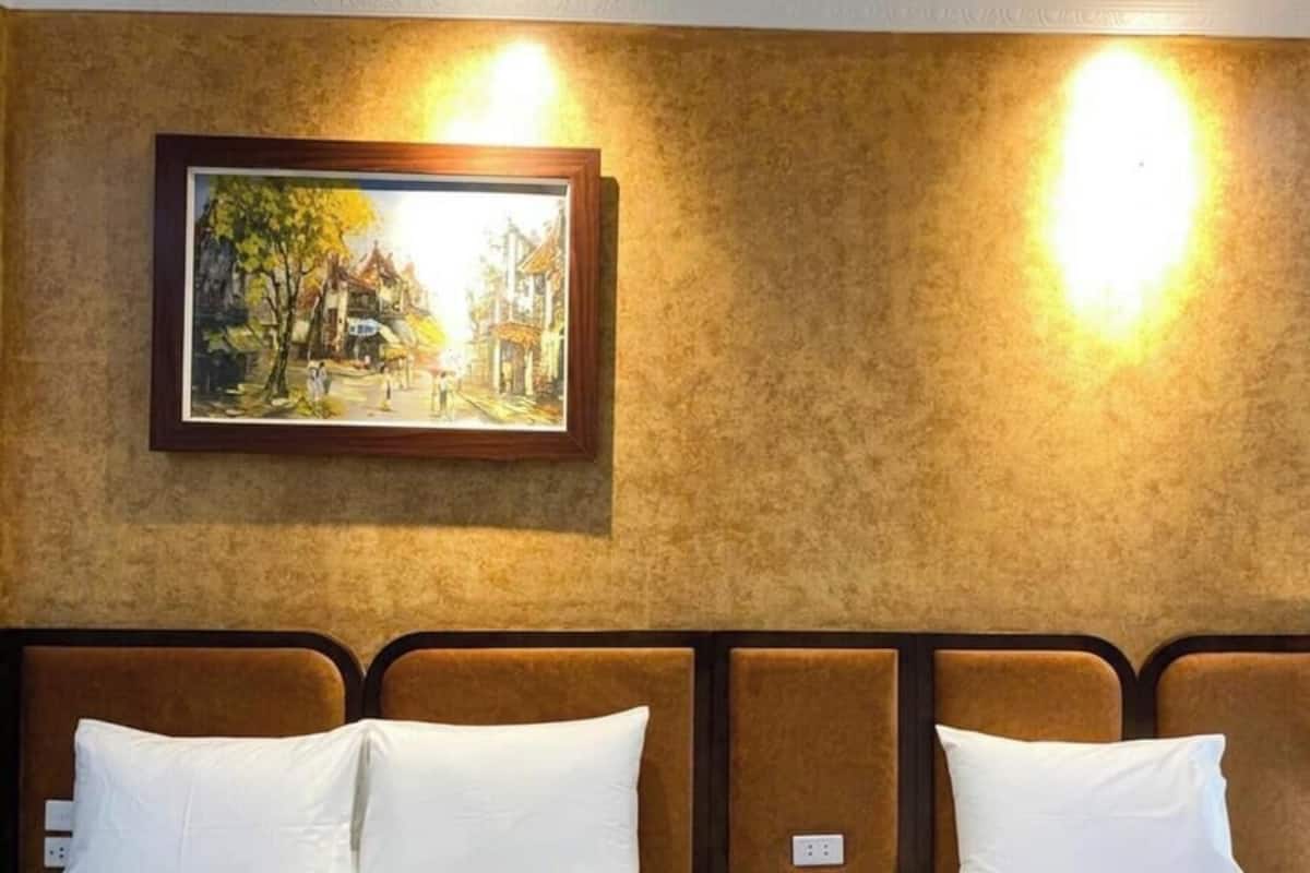 A hotel room with a bed, a framed painting on the wall, and two wall-mounted lights.