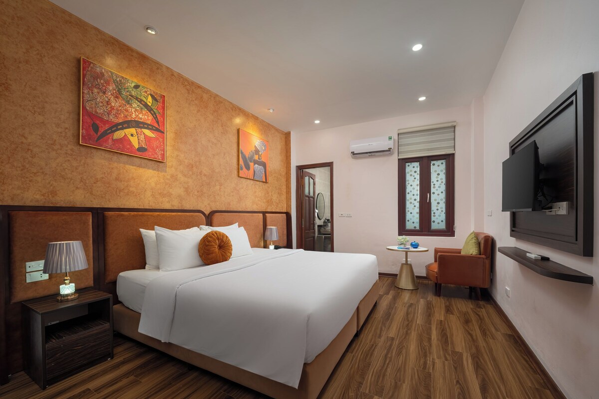 Ein Hotelzimmer mit einem großen Bett, einem Fernseher, einem kleinen Tisch und Kunstwerken an den Wänden.
