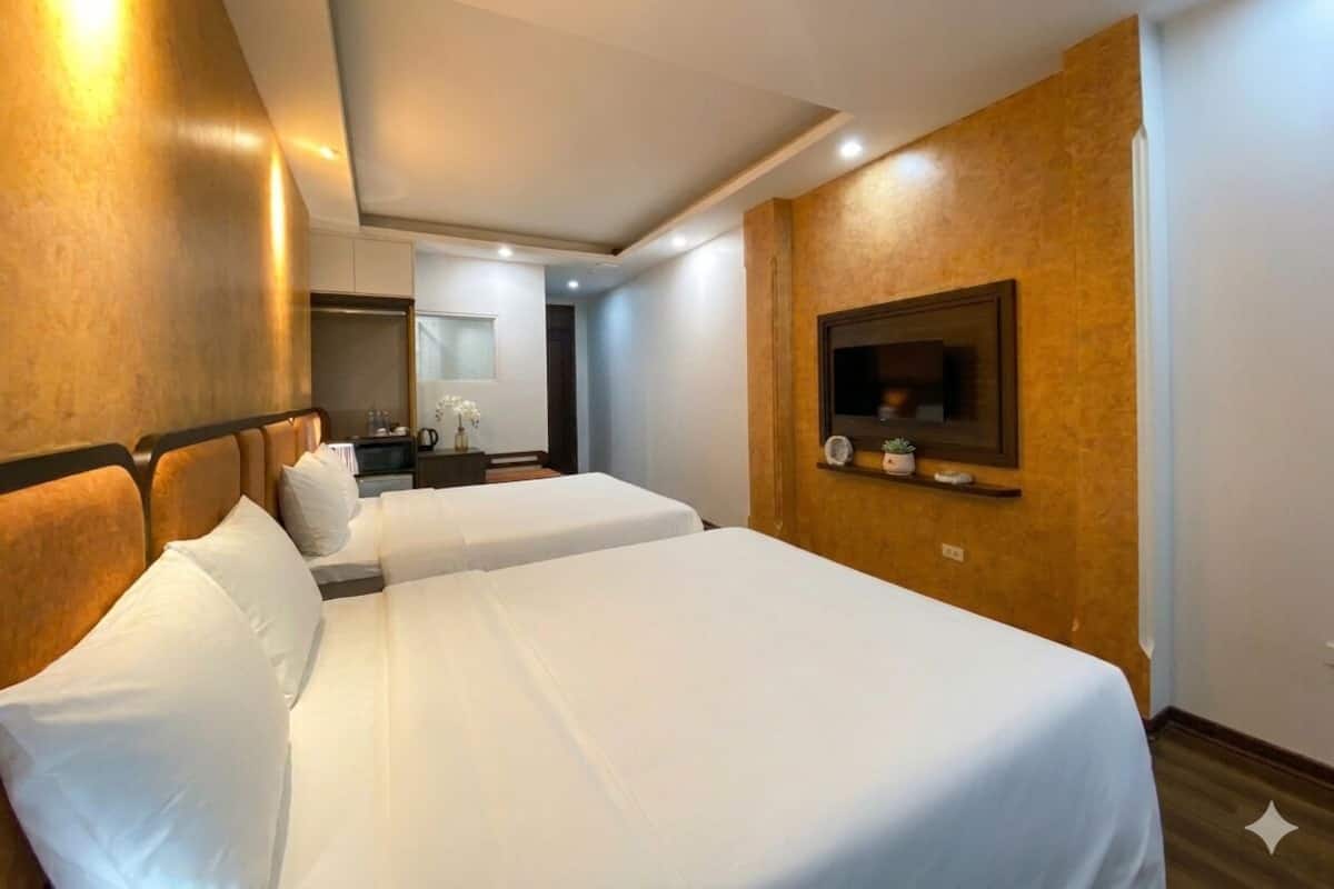 A hotel room with two beds, a bedside table with a lamp, a mirror, and a small shelf with decorative items.