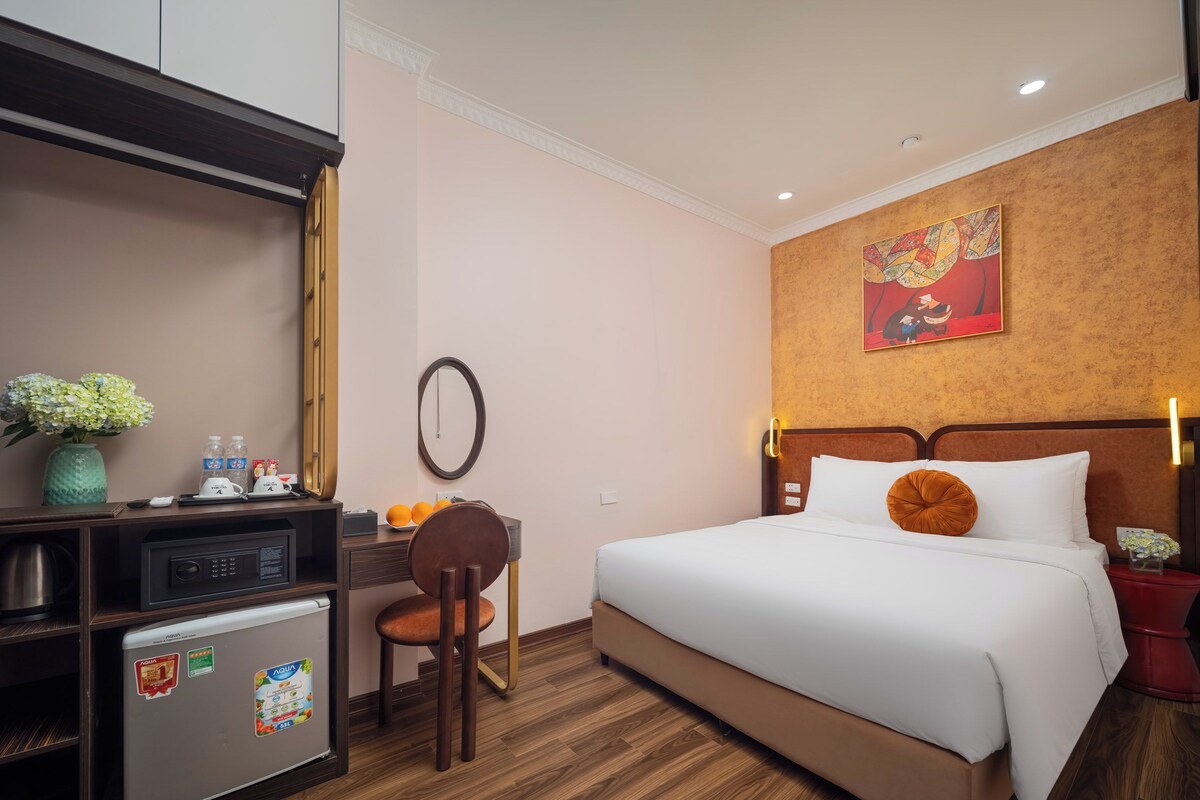 Ein Hotelzimmer mit einem Bett, einem Schreibtisch mit Kühlschrank, einem Sessel, einem Spiegel und einem Wandbild.