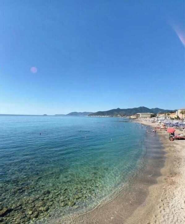 Una spiaggia con acque cristalline, una riva sabbiosa e edifici sullo sfondo.
