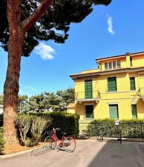 Un edificio giallo con un balcone, una bicicletta e un albero.