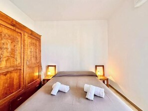 Una camera da letto con un'armadio in legno, due comodini con lampade e due asciugamani piegati con cura sul letto.