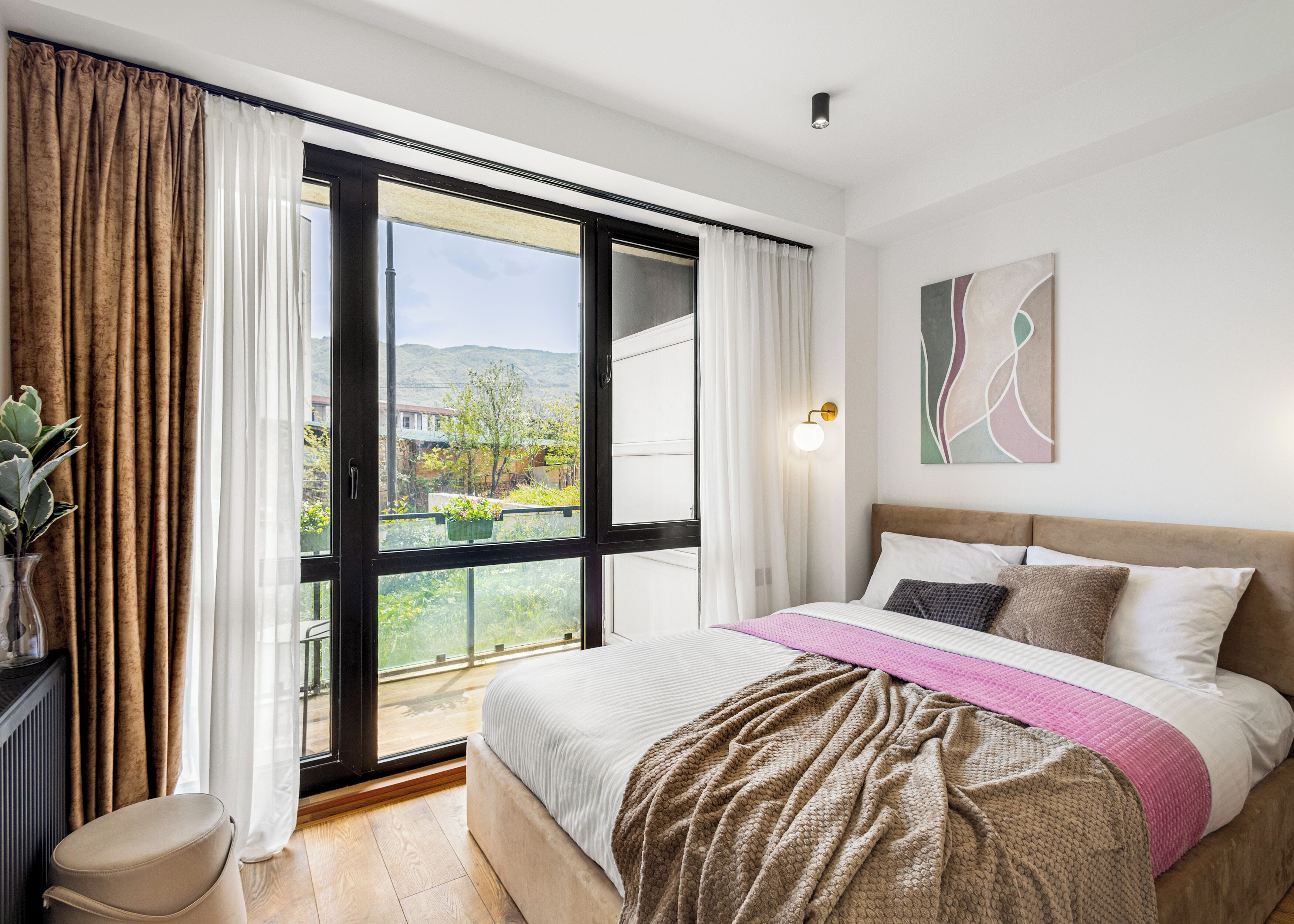 Ein Schlafzimmer mit Bett, Vorhängen an einem Fenster, einem Nachttisch und einer Wandleuchte.