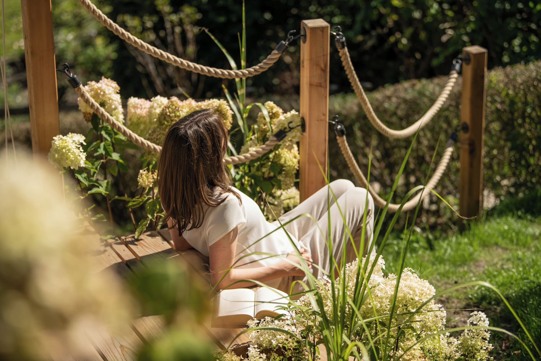 A person sitting on a wooden deck surrounded by greenery and ropes.