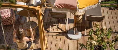 Una terraza de madera con mobiliario de mimbre, incluyendo un columpio, sillas y una mesa.