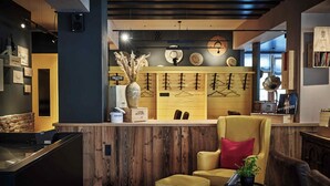 Una zona de bar con mostrador de madera, un sillón amarillo y una pequeña mesa con una planta.