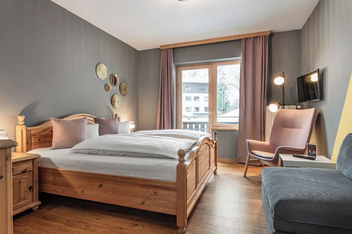 A bedroom with a wooden bed, a desk, a chair, and a window with curtains.