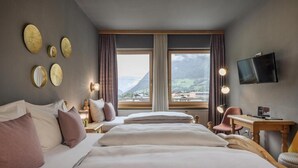 Habitación de hotel con dos camas, un escritorio, una silla, un televisor y un amplio ventanal con vistas a la montaña.