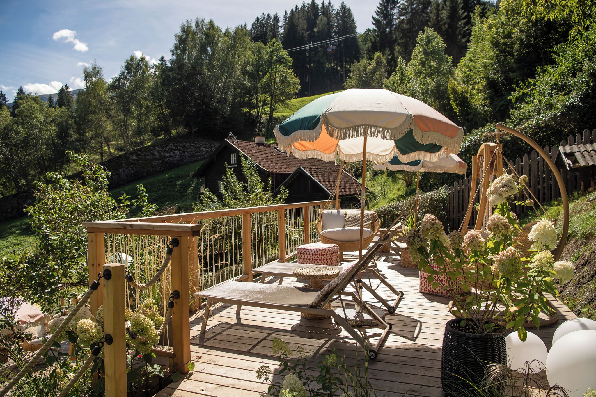 Una terraza de madera con sillones de descanso, una hamaca y un paraguas decorativo.