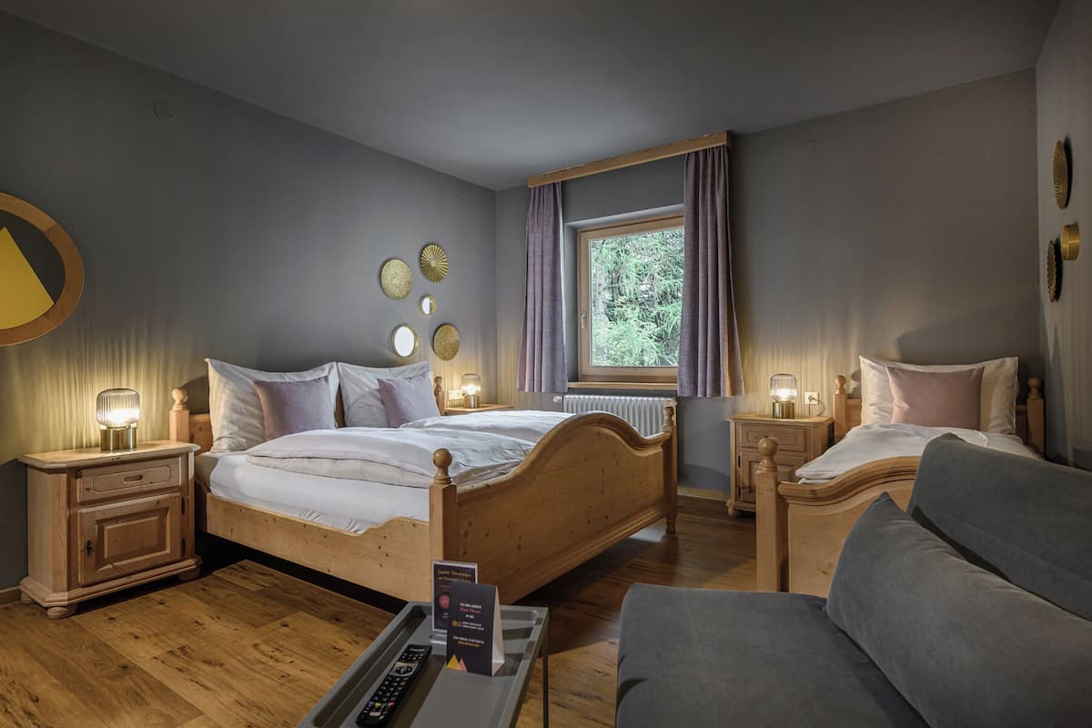 A bedroom with a wooden bed, two bedside tables, a nightstand, a grey armchair, and a window with curtains.