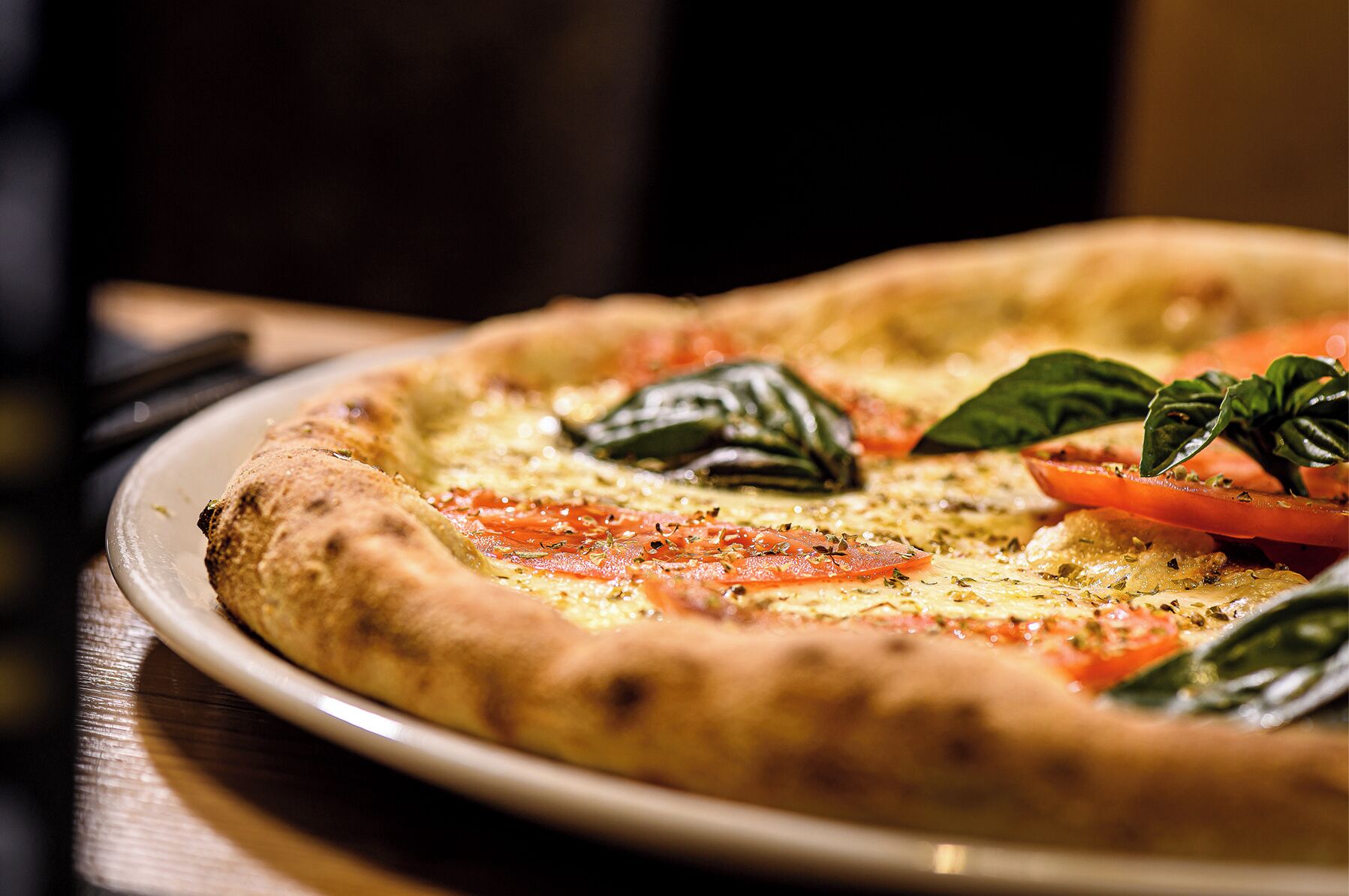 A pizza on a plate with visible toppings and a basil leaf garnish.
