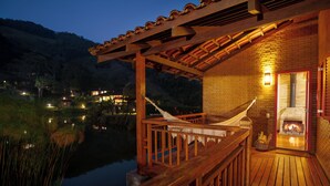 Una terraza de madera con una hamaca, una chimenea y vistas a un lago al anochecer.
