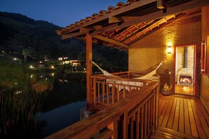 Una terraza de madera con una hamaca, una chimenea y vistas a un lago al anochecer.