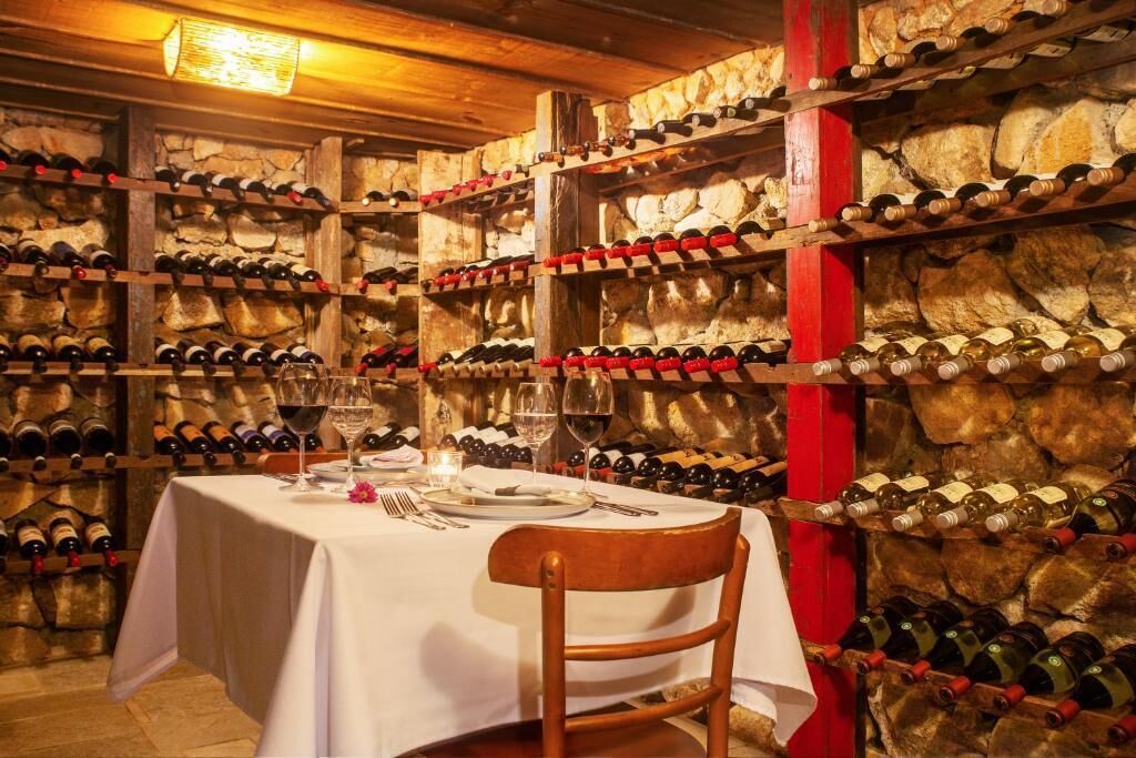 A wine cellar with a table set for dining, surrounded by stone walls and wooden racks of wine bottles.