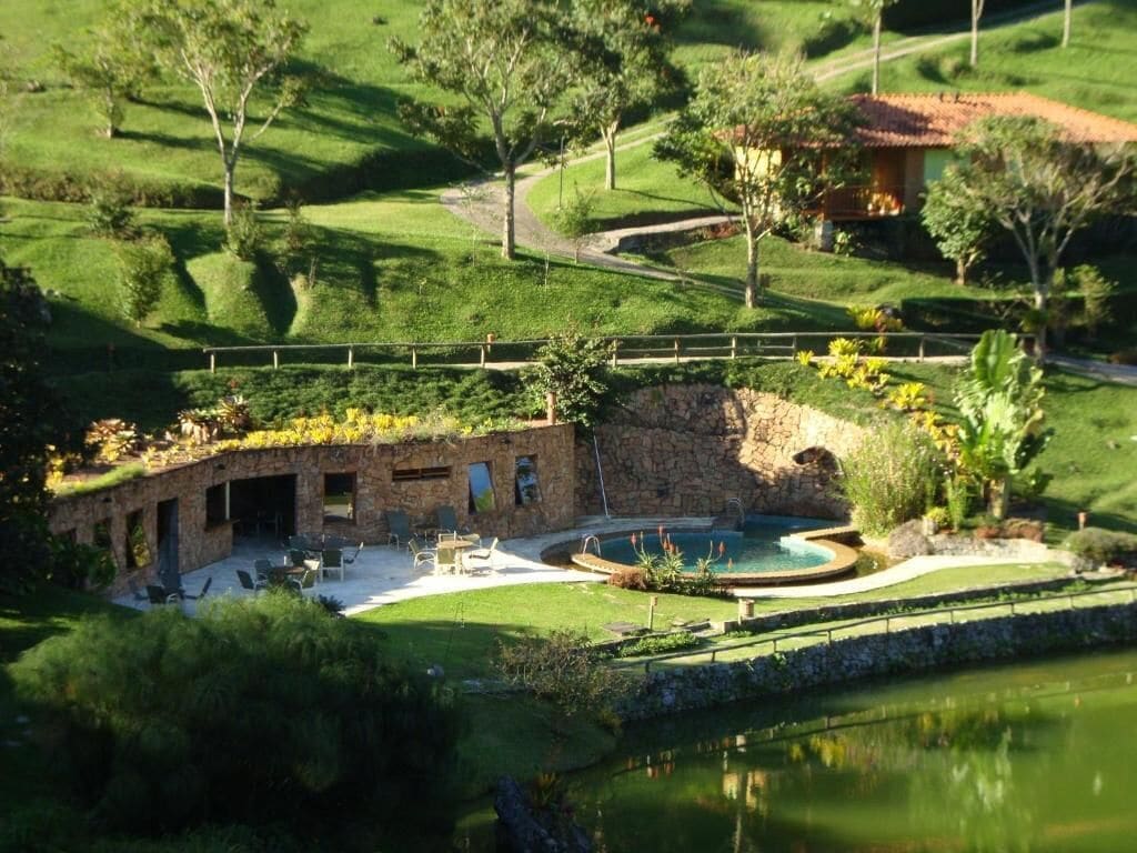 Un edificio de piedra con piscina, rodeado de abundante vegetación y un estanque.