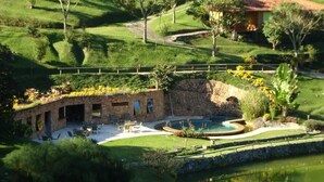 Un edificio de piedra con piscina, rodeado de abundante vegetación y un estanque.