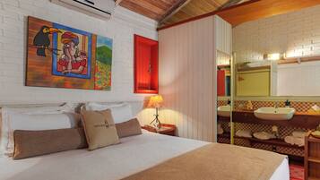 Une chambre d’hôtel avec un lit, un tableau, une porte rouge, une table de chevet, une lampe, un miroir et une salle de bain avec un lavabo et un porte-serviettes.