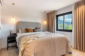 A modern bedroom with a large bed, a nightstand, a bedside table, and a window with curtains. - Luxury Golf Townhouse in Aloha with Pool & Garden (Marbella)