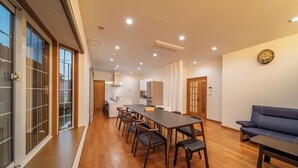 A spacious living area with a long dining table, multiple chairs, a sofa, and a kitchen in the background. - KINNOKA YUNOYADO (Yufu)