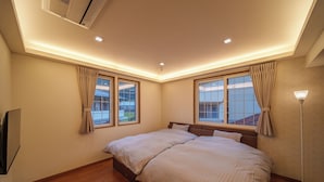Une chambre à coucher avec un grand lit, deux fenêtres, un ventilateur de plafond et un lampadaire.