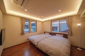 Un dormitorio con una cama grande, dos ventanas, un ventilador de techo y una lámpara de pie.