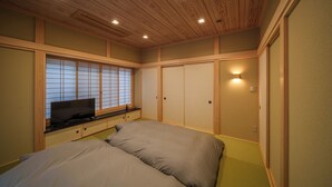 A bedroom with a bed, a TV on a low shelf, wooden paneling, and a sliding door. - KINNOKA YUNOYADO (Yufu)