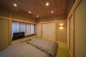 A bedroom with a bed, a TV on a low shelf, wooden paneling, and a sliding door. - KINNOKA YUNOYADO (Yufu)