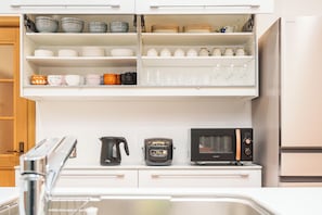 Una cocina con armarios blancos, microondas, cafetera y diferentes utensilios.