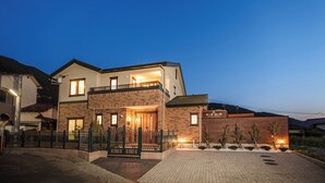 Une maison à deux étages avec un balcon, une entrée sécurisée par un portail et une allée pavée.