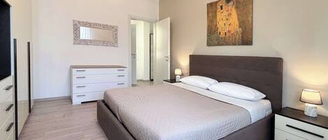 A bedroom with a bed, bedside tables, a dresser, a mirror, and a painting on the wall.