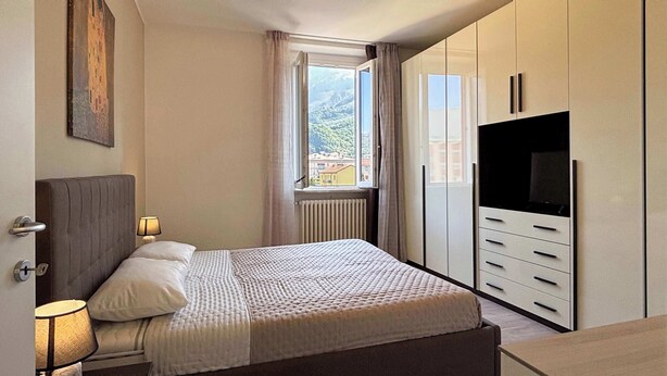 Un dormitorio con cama, lámparas de noche, ventana con vistas, armario y televisor.