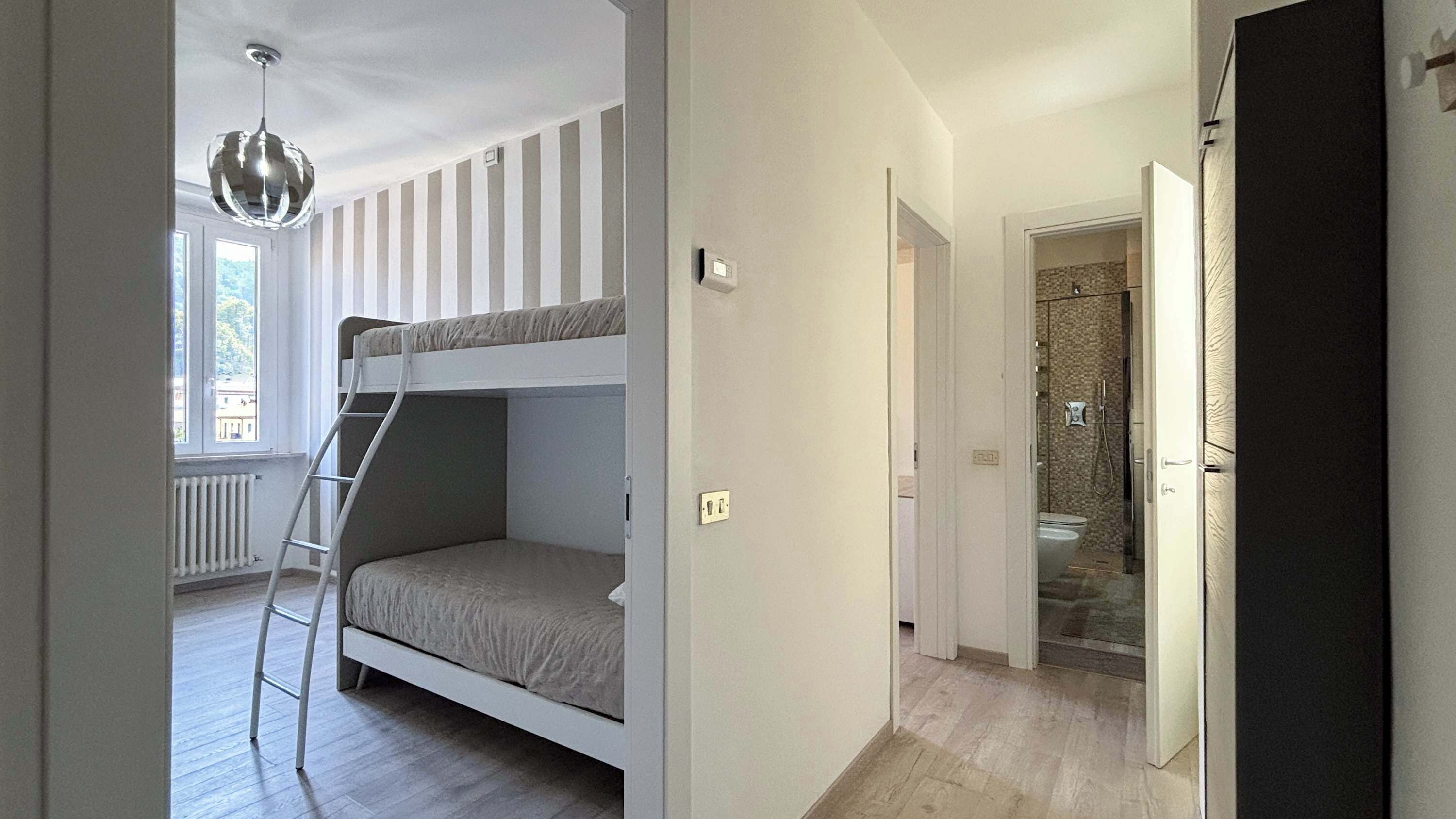 A room with bunk beds, a ladder, a shower, and a view of the outside.