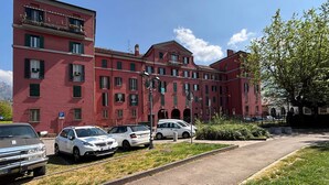 Un edificio rojo de varios pisos con un estacionamiento al frente, varios coches aparcados y un cielo despejado.