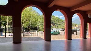 Un espacio al aire libre cubierto con arcos, suelo empedrado y vista a un estacionamiento con autos y una montaña al fondo.