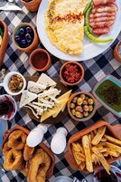 Variedad de alimentos, como una tortilla, tomates, aceitunas, queso y pan.