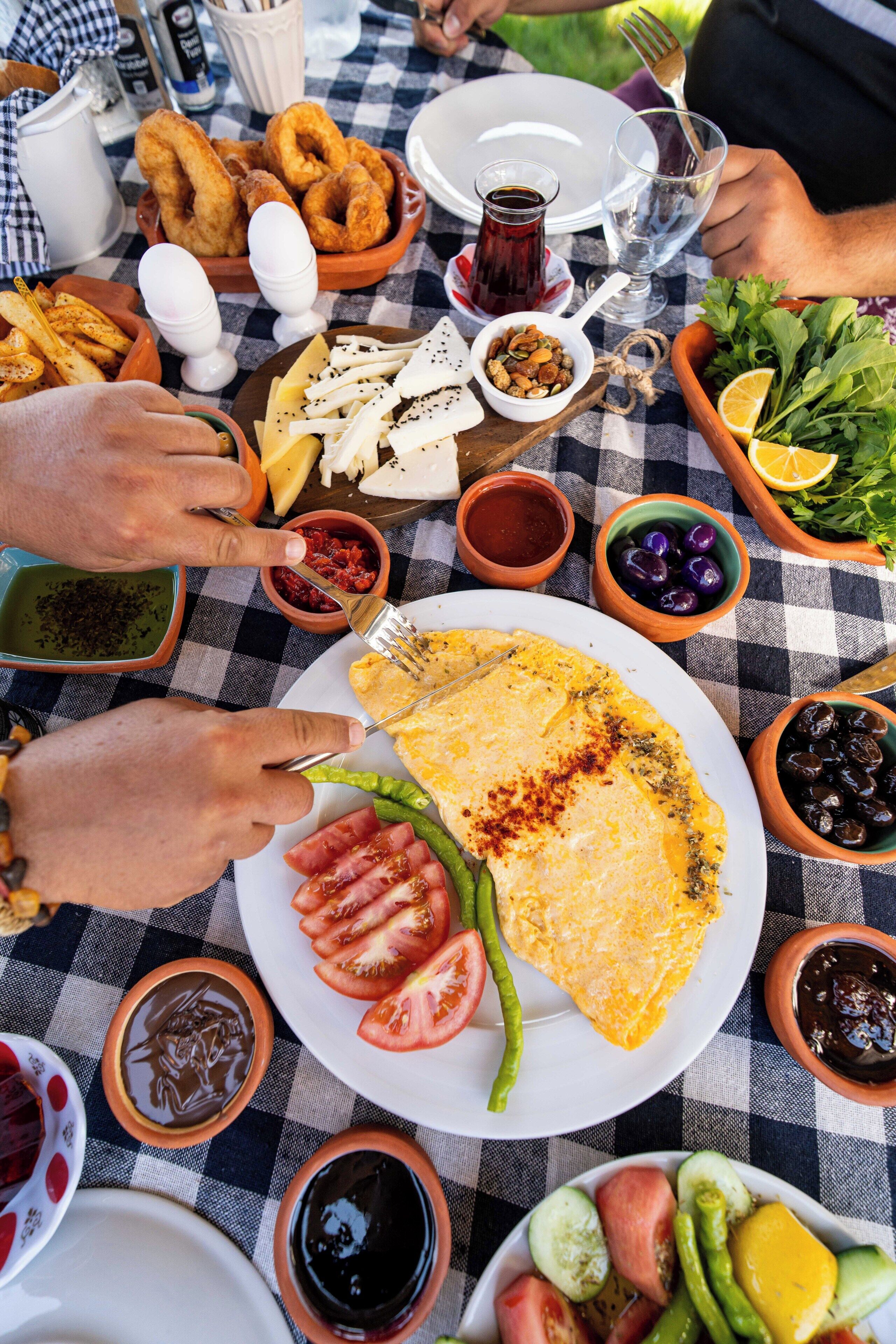 A table set with various dishes including a plate of omelette, tomatoes, green peppers, and olives.