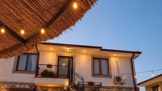 Un bâtiment à deux étages, avec un escalier menant à l’étage supérieur, une enseigne indiquant « HOSGELDINZ » et un espace restaurant doté de tables en plein air.